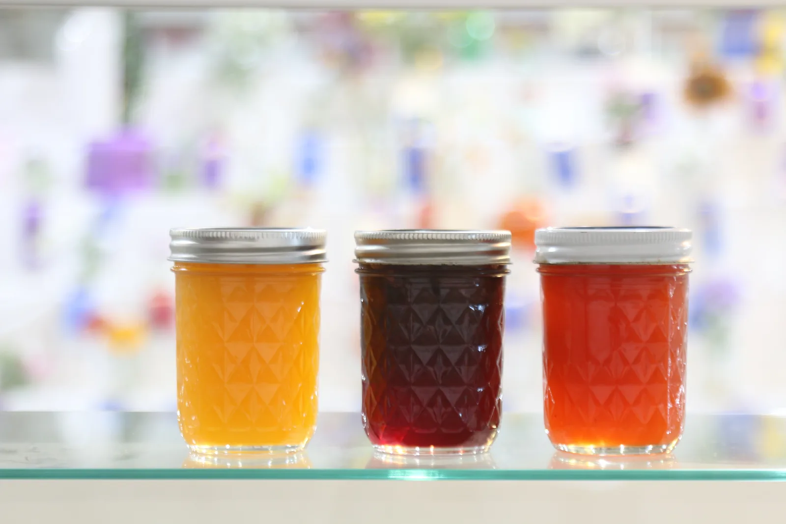 Three glass jars of home-canned jelly on a glass shelf